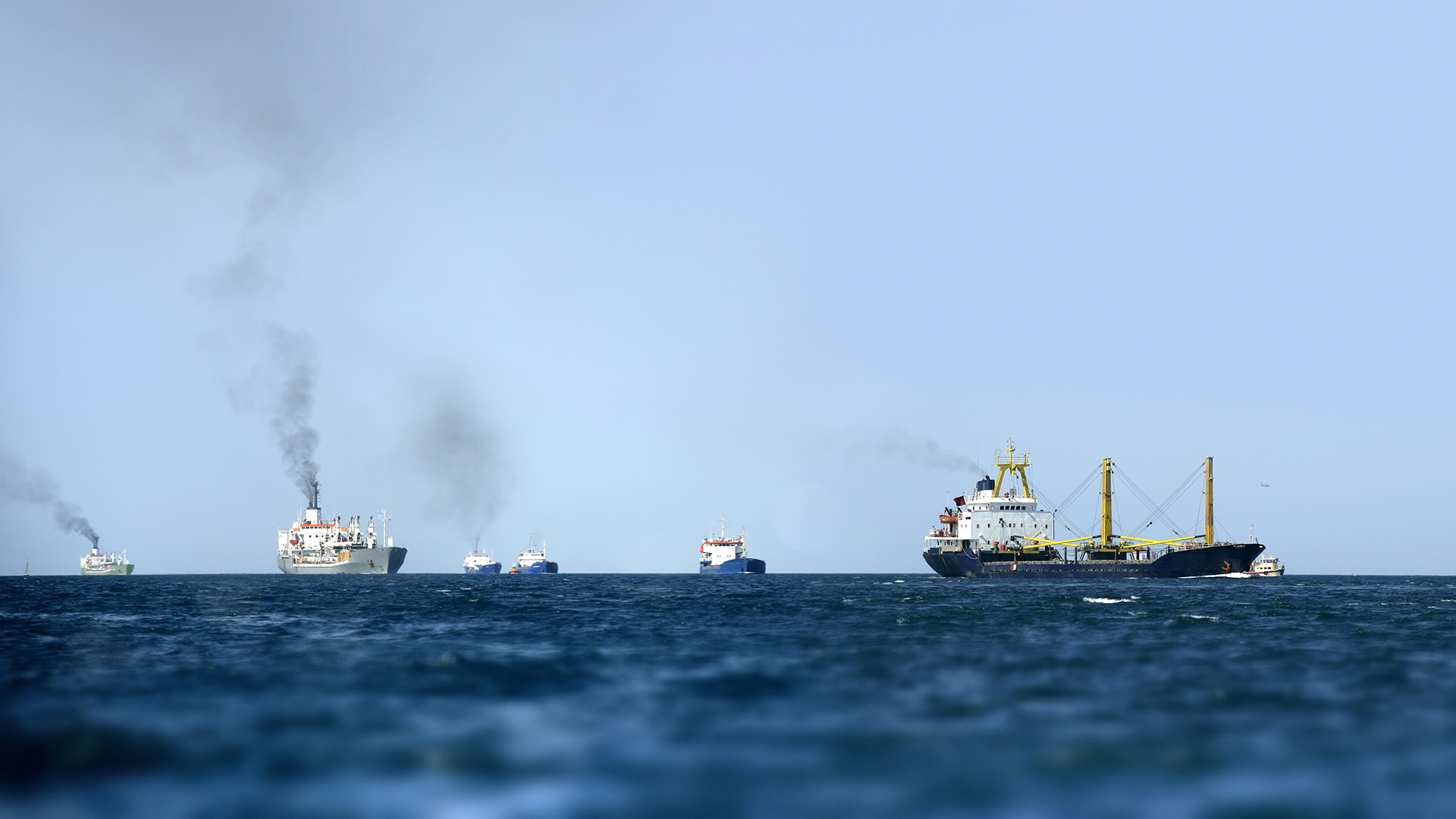Ships on the sea with plumes of smoke coming out of their smokestacks