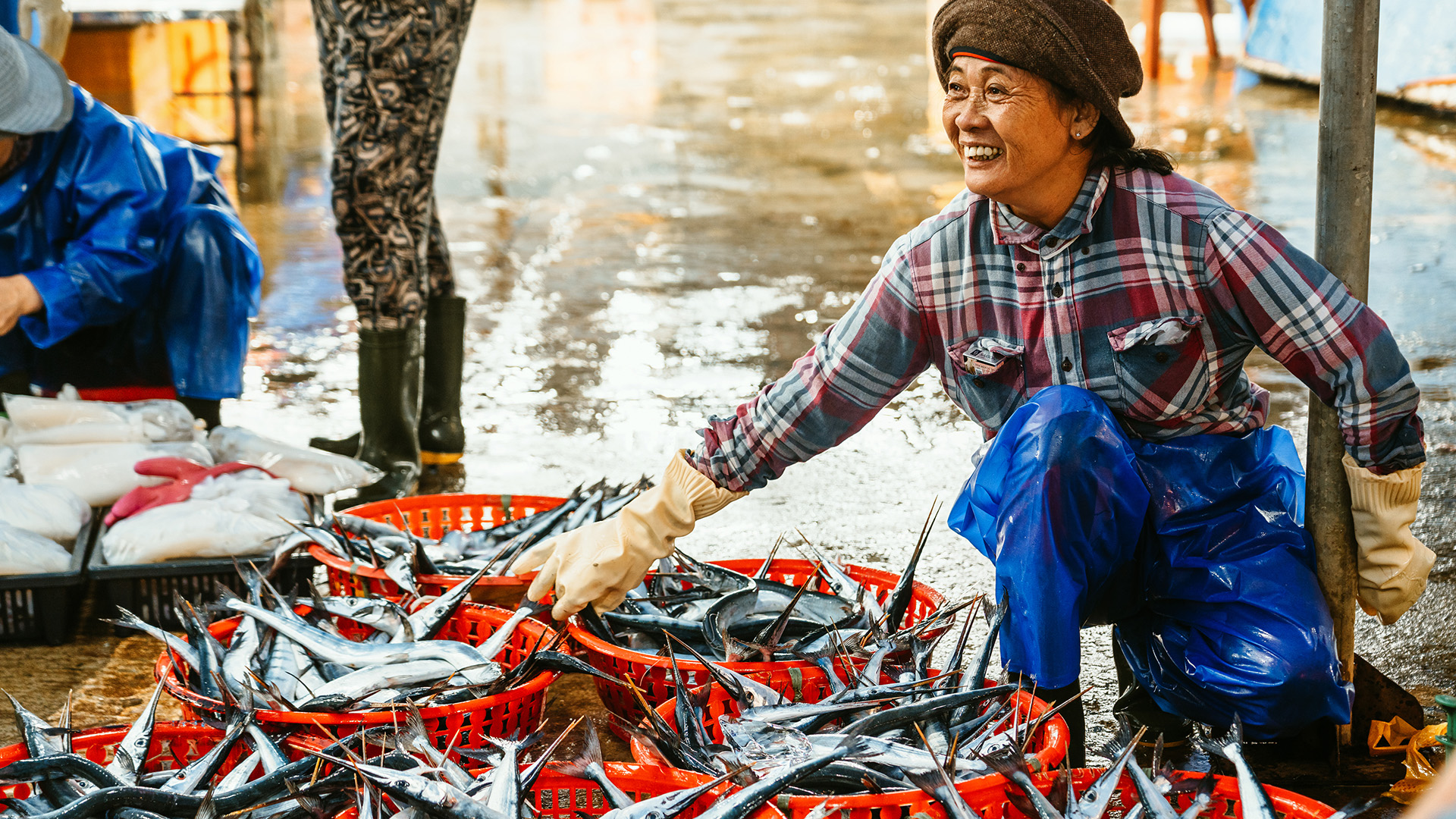 A smiling woman sells baskets of fish at a coastal market in Vietnam