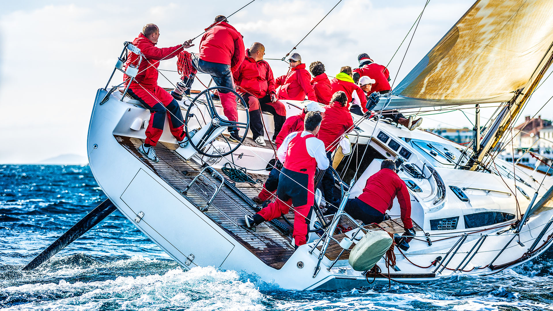 A group of sailors in bright red jackets guide a sailboat through strong winds during a regatta
