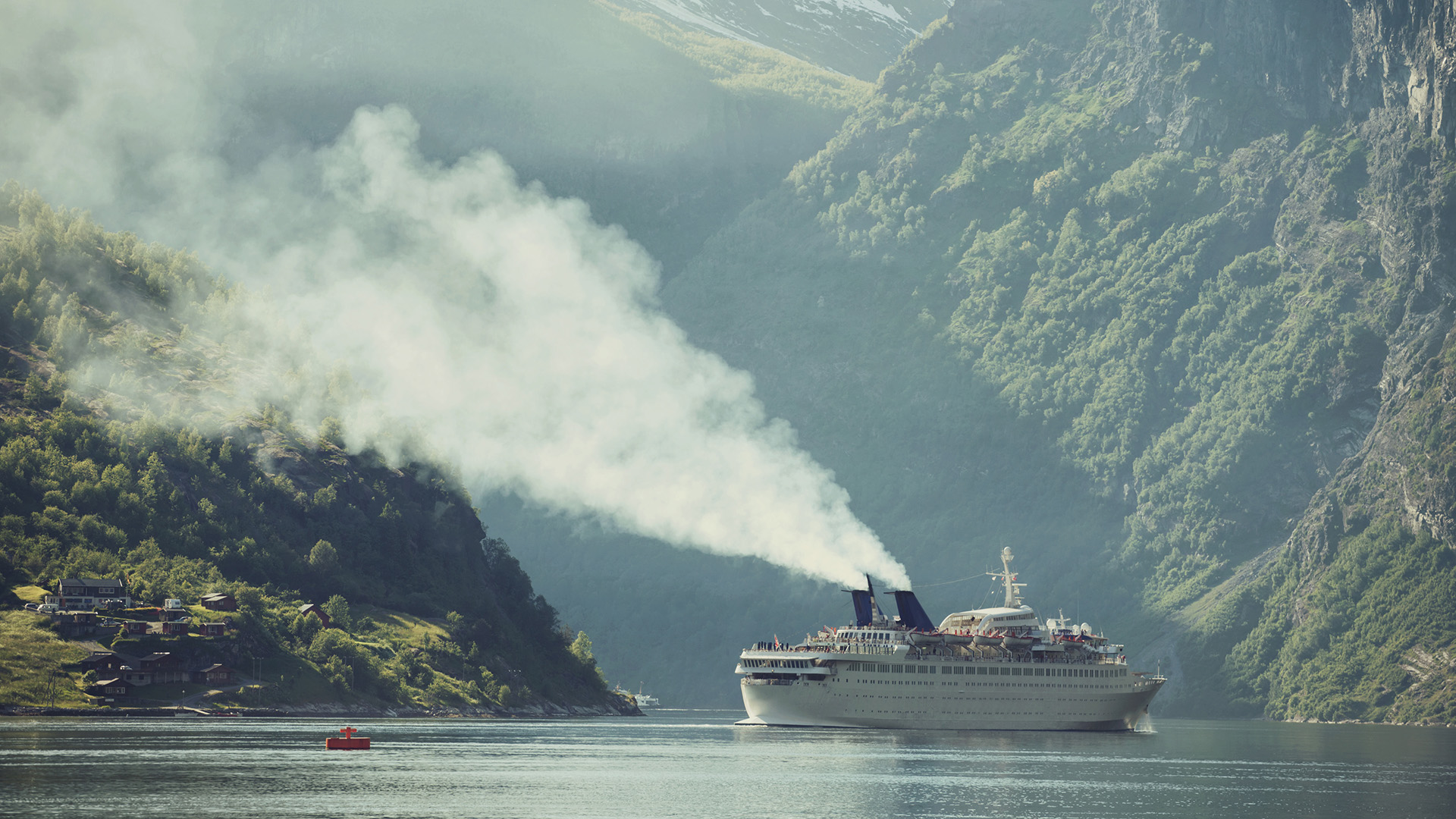 A cruise ship belches smoke into a majestic fjord