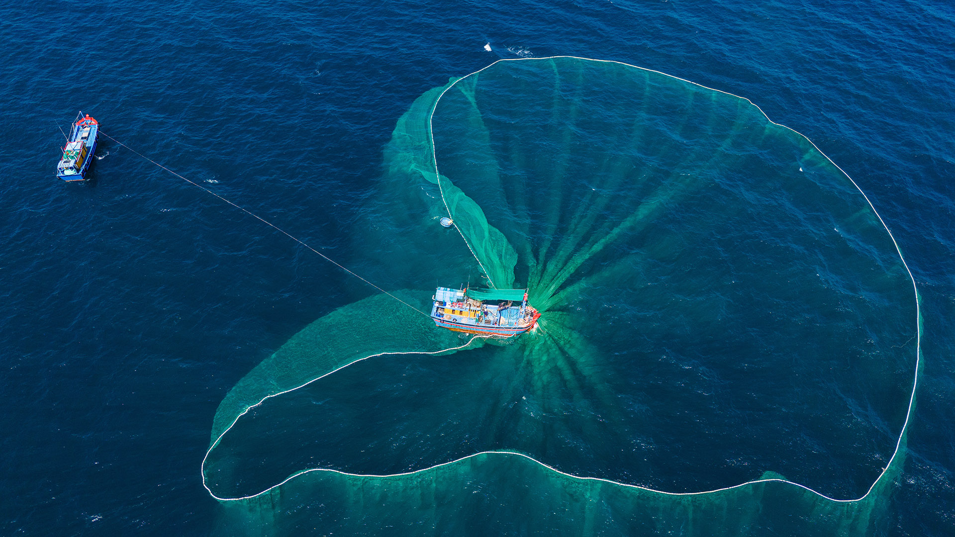 A Thai fishing boat collects its large turquoise net from the water
