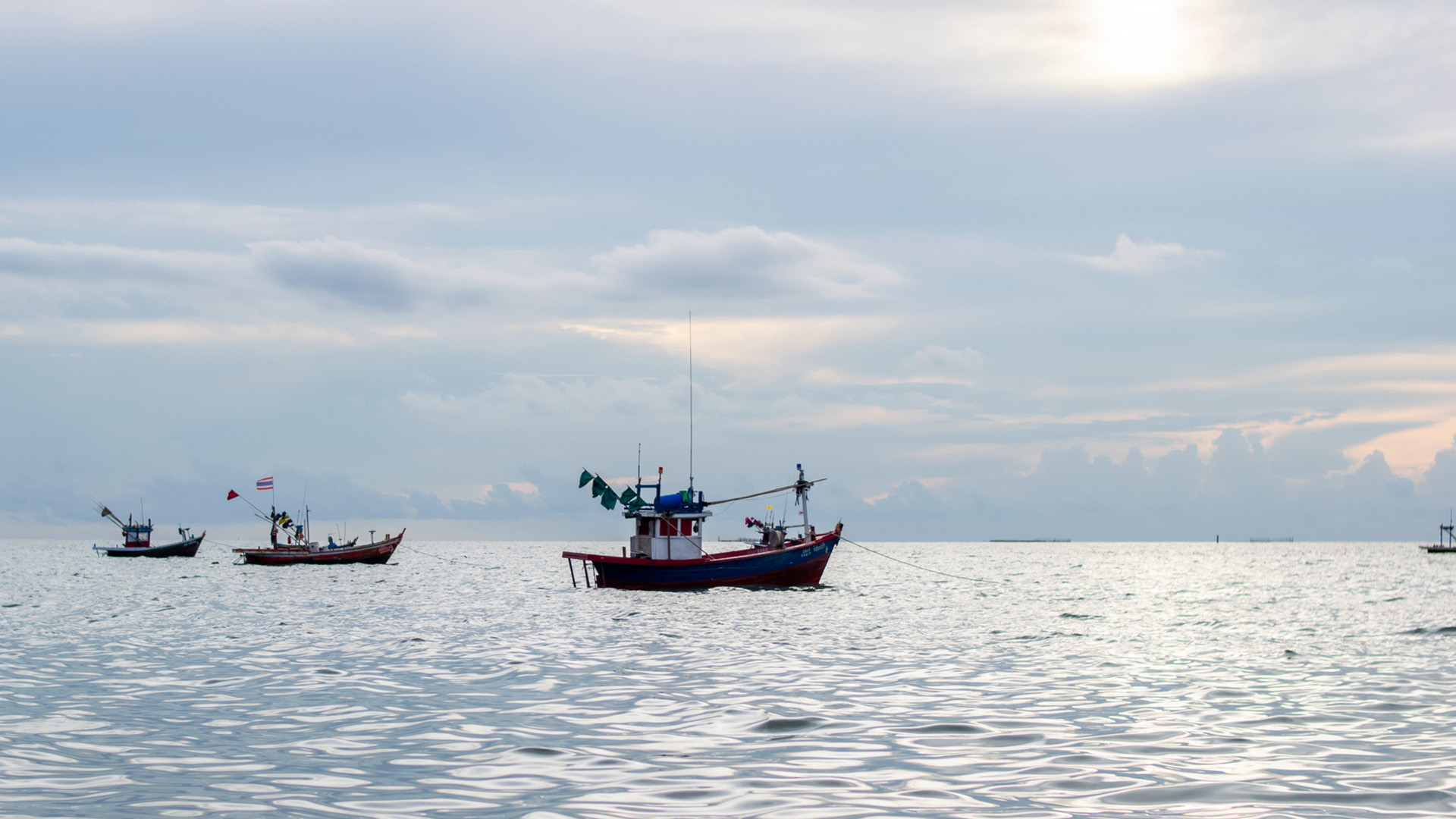 Thai fishing boats on a silver ocean with cloudy sky