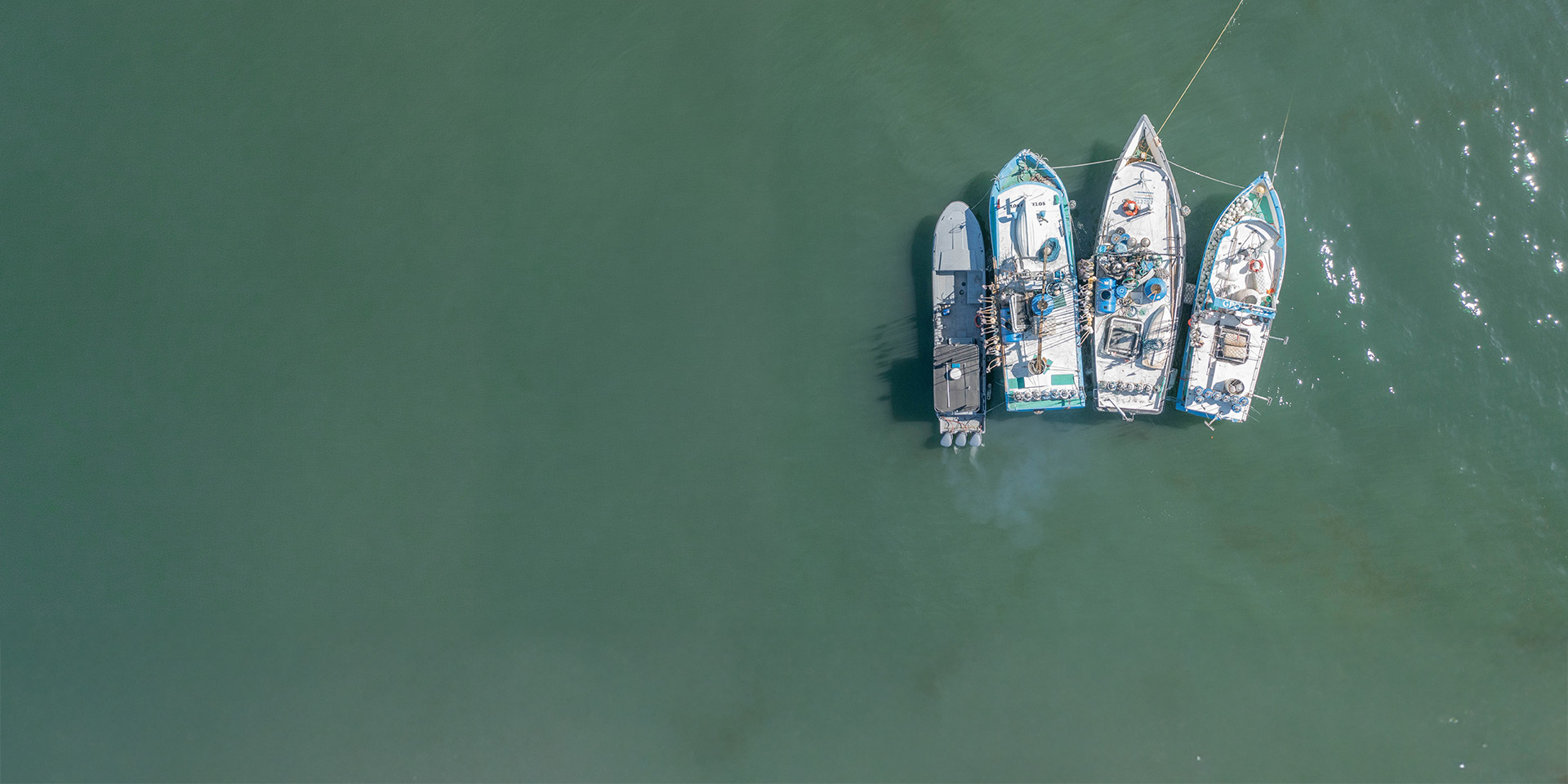 An enforcement patrol boat pulls up alongside a trio of commercial fishing vessels on a dark turquoise ocean