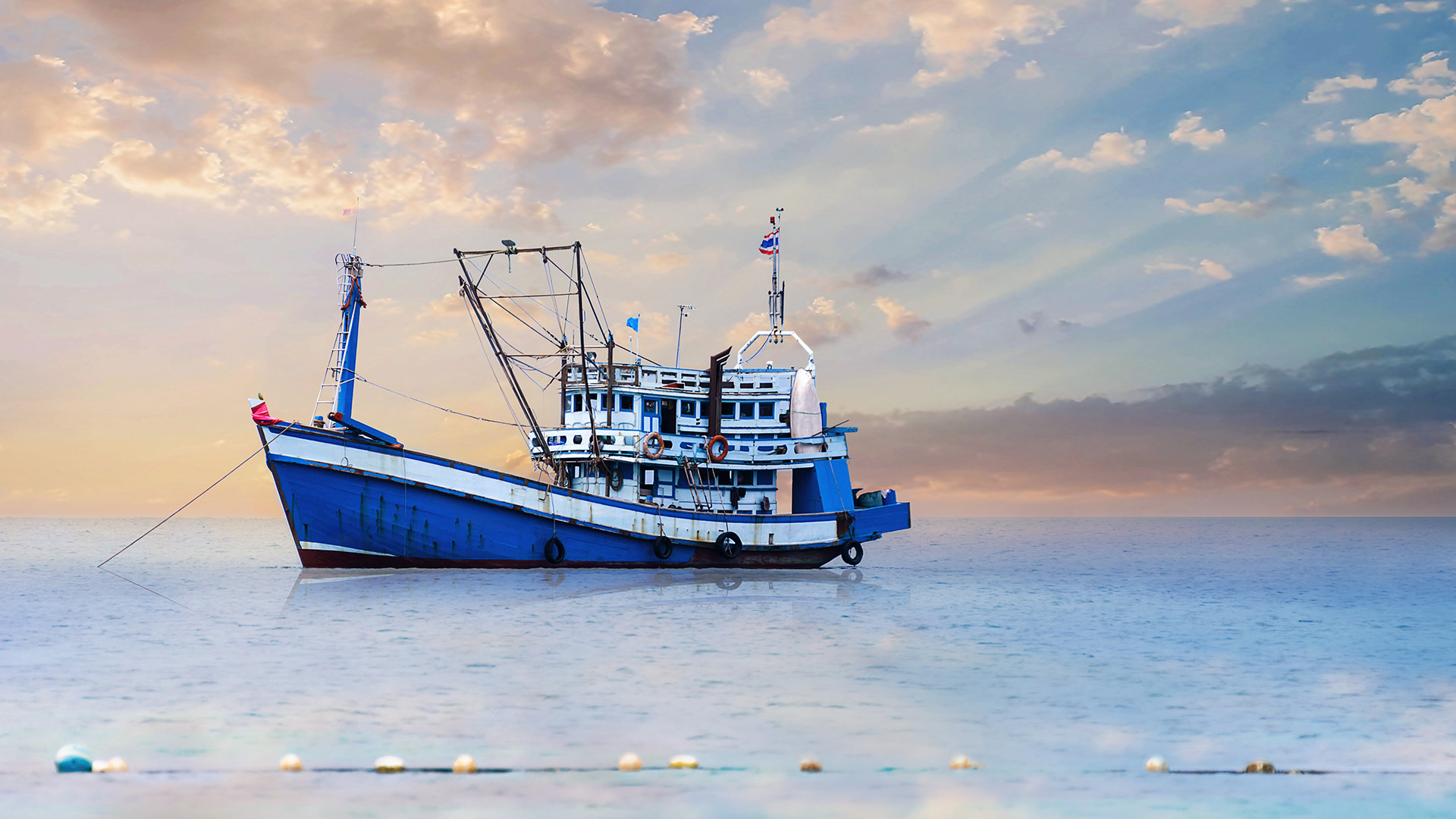 A bright blue and white fishing boat anchored at sunrise
