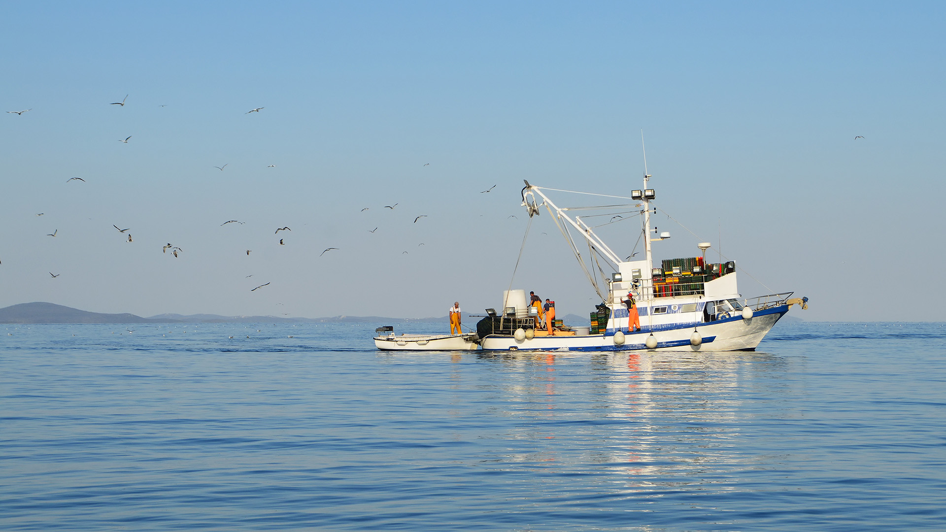 Deckhands work on a commercial fishing boat on a calm day with glassy ocean water