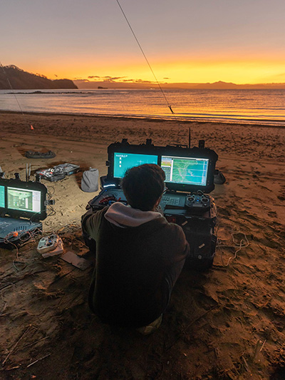 A drone operator looks at screens at the beach